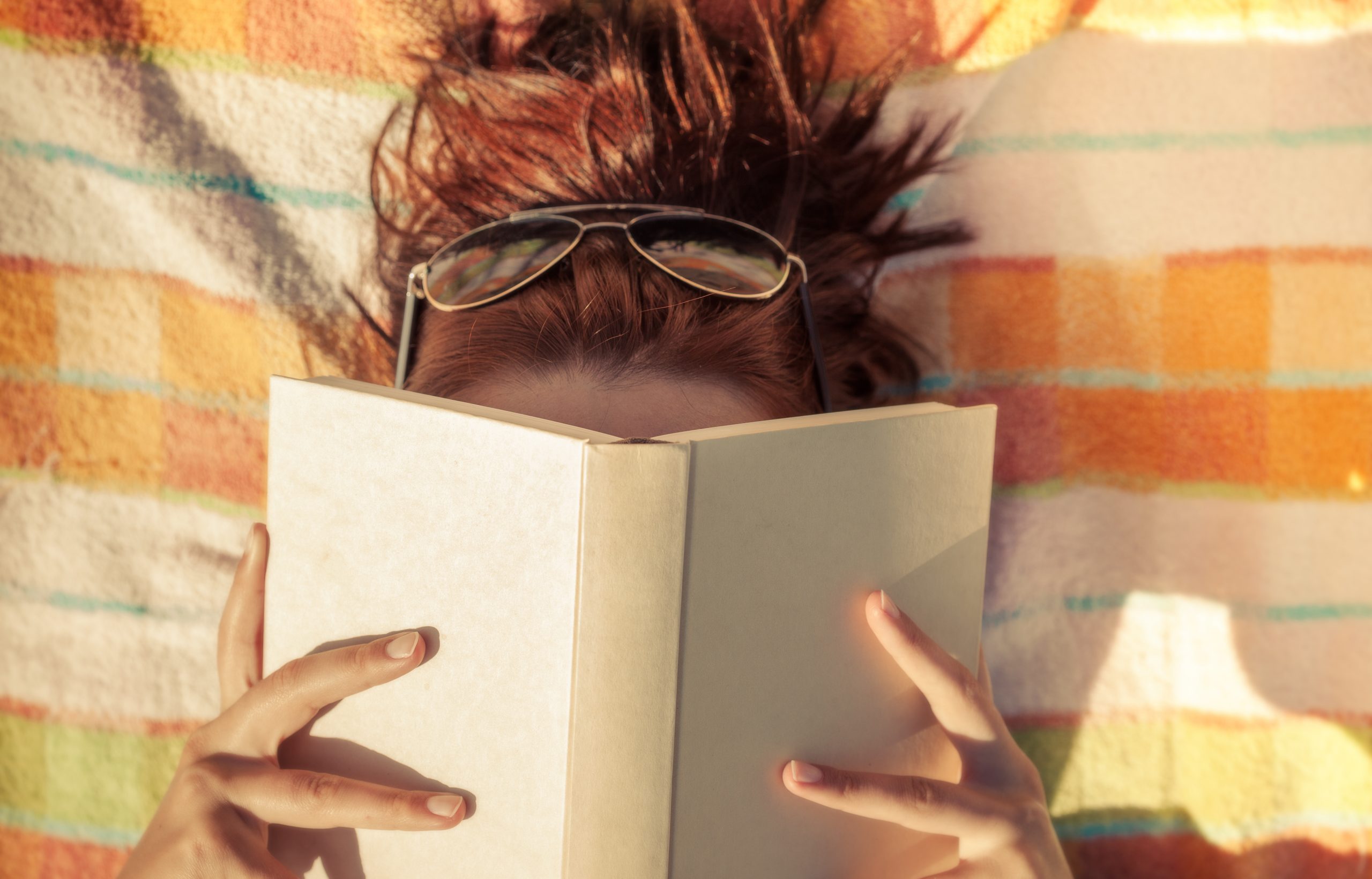Woman with sunglasses with book covering her face.