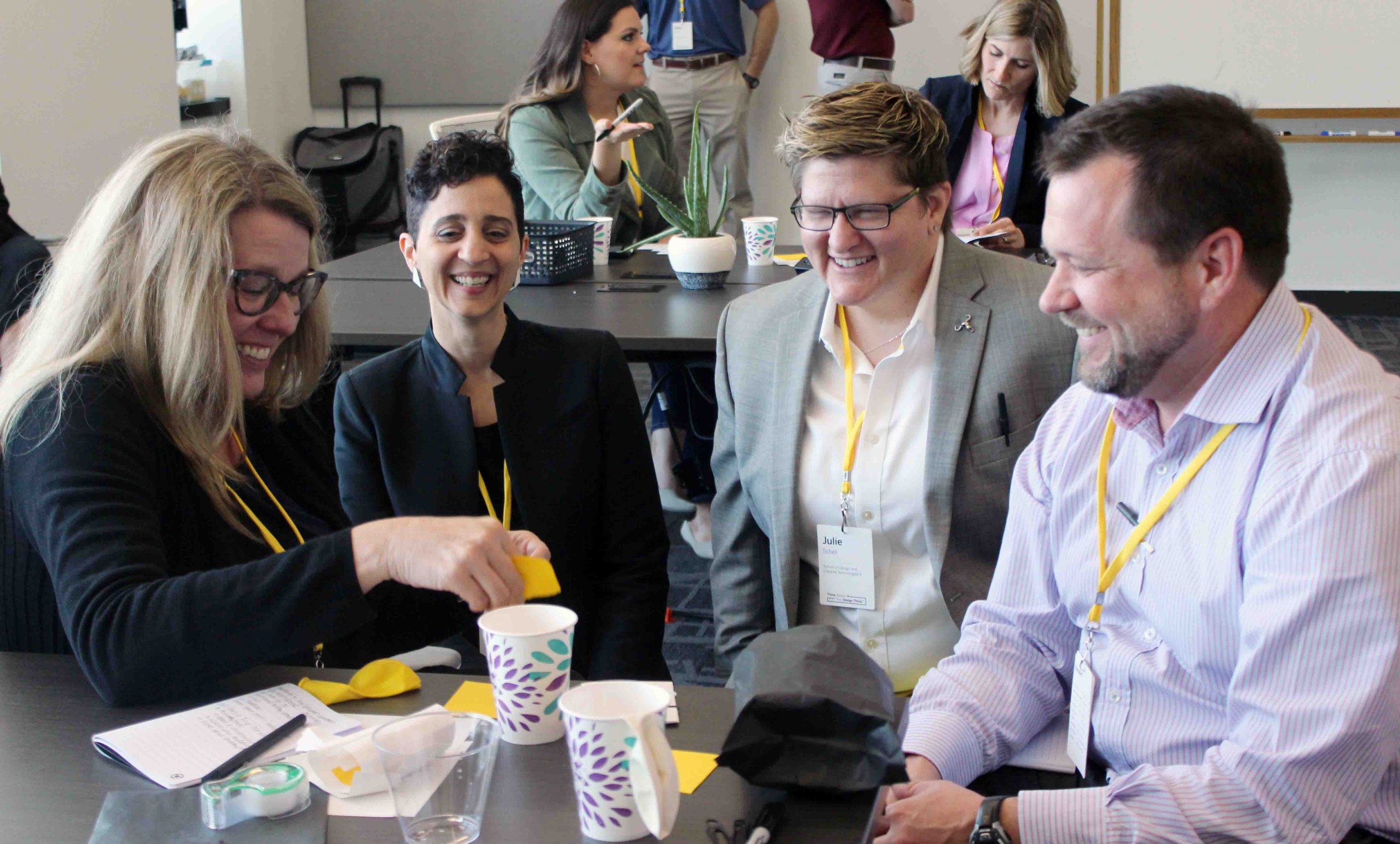 A group of four people with yellow lanyards around their necks laughing and working together during a Design Thinking workshop.
