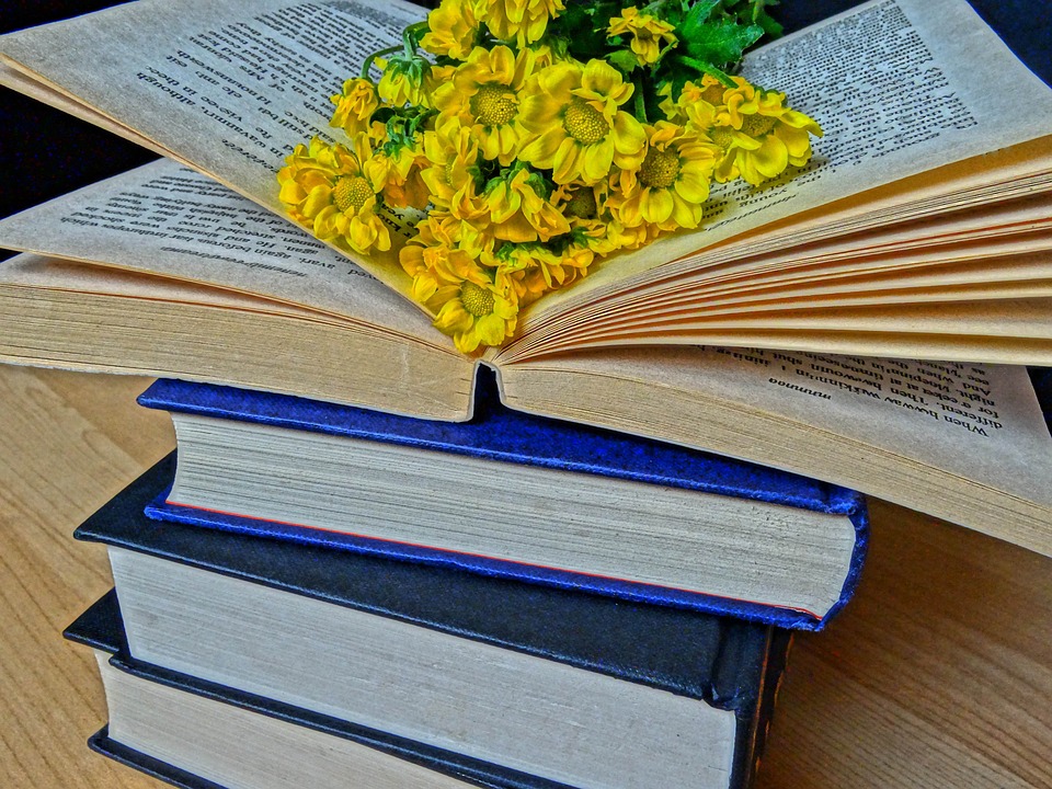 Stack of books. Top book is open with yellow flowers in center.