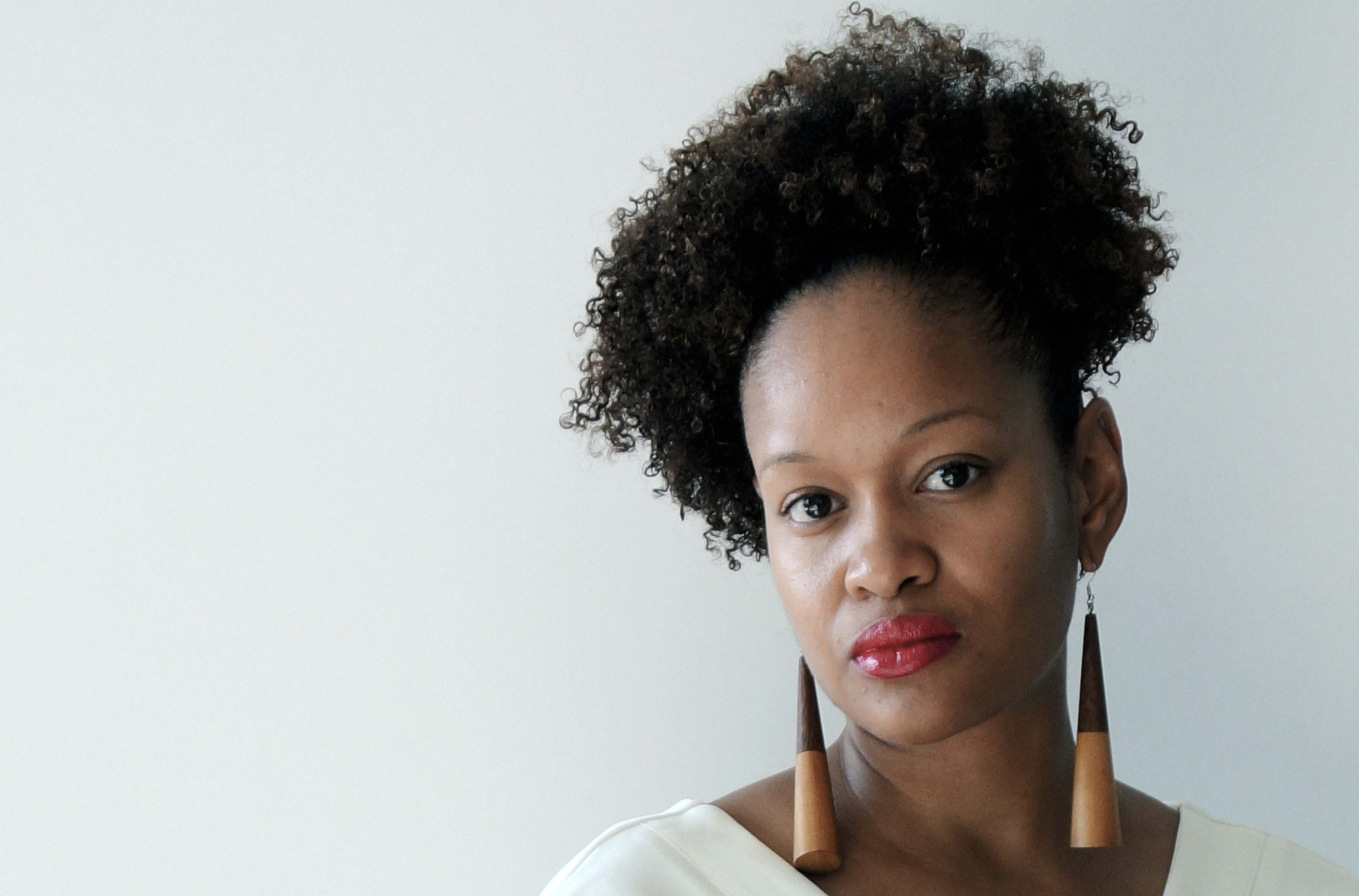 Ja'nell Ajani in white, wearing large geometric earrings and a white dress.